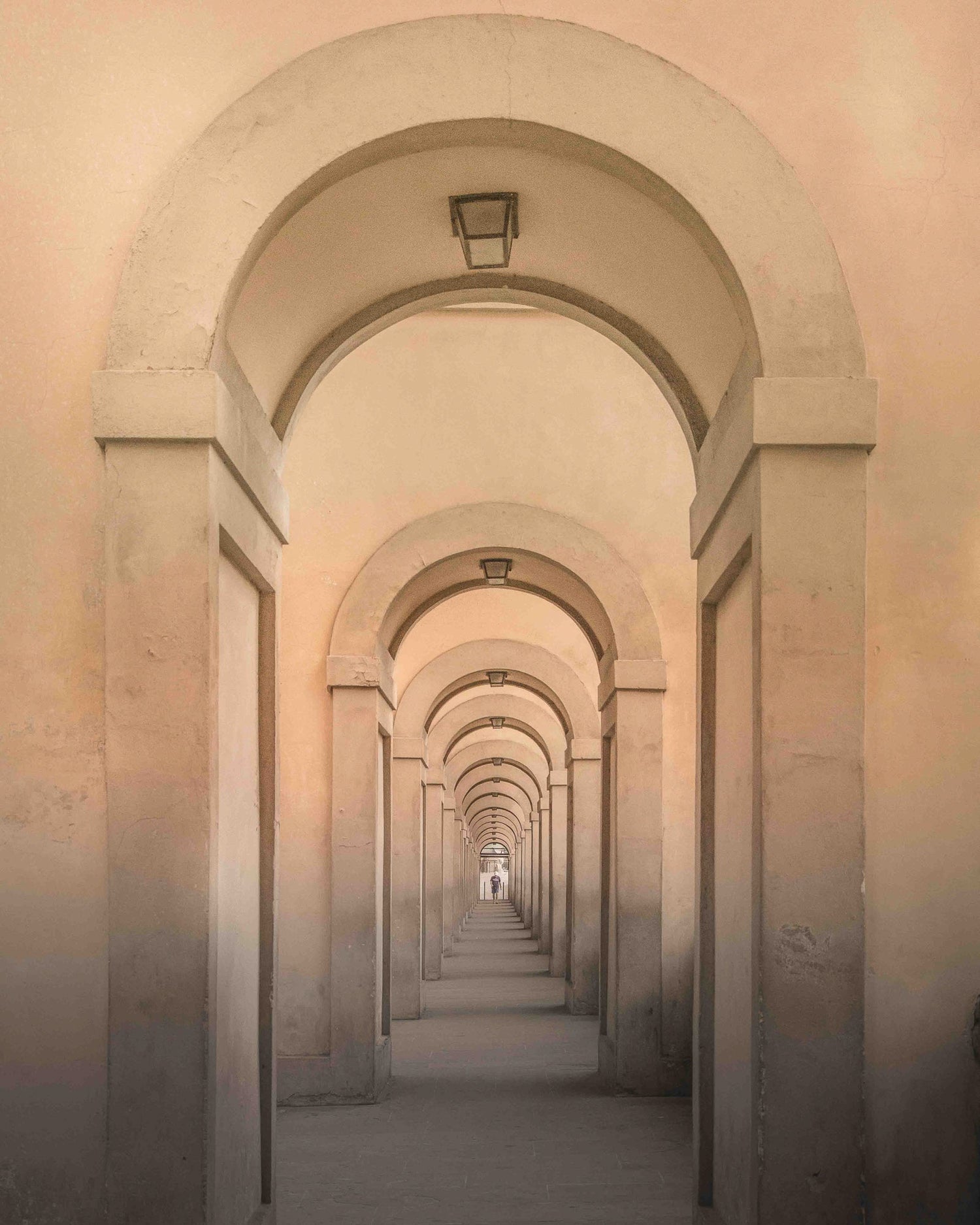 Warm-toned Florence arches leading to a distant figure in soft light